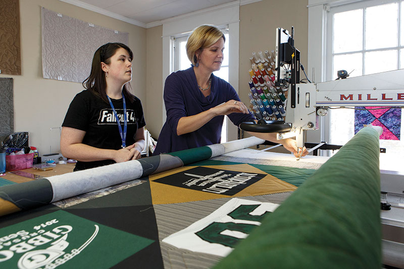 Carrie Hauser, left, and Julianne Walther consult at the long-arm quilting machine. In addition to selling fabric and supplies, the shop provides quilting services for customers.